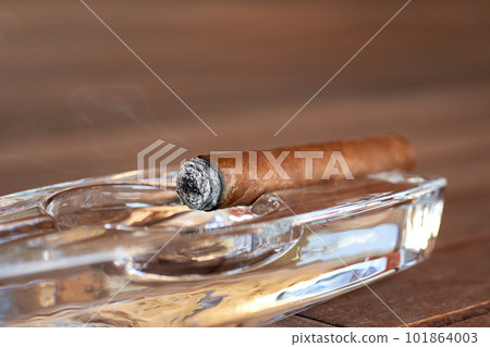 Burning Cuban cigar in a glass ashtray 101864003