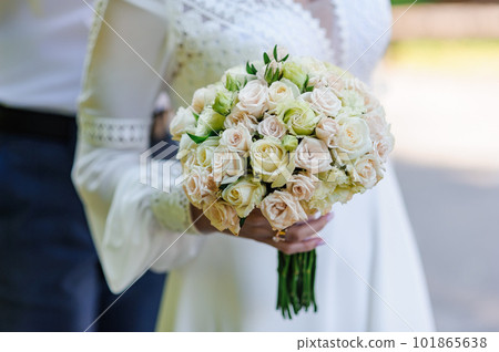 Bouquet of white roses in the hands of the bride. Bride's bouquet of white flowers in the hands of a woman Bouquet of white roses in the hands of the bride. Bride's bouquet of white flowers in the hands of a woman 101865638