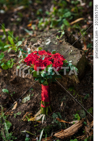 Two golden wedding rings on a stump, in the background a bouquet with red roses Two golden wedding rings on a stump, in the background a bouquet with red roses 101865706