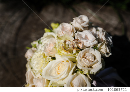 Two golden wedding rings on a stump, a bride's bouquet of flowers in the background 101865721