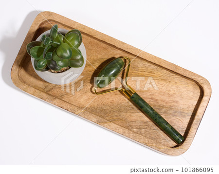 Jade facial massager, an item for cosmetic procedures on a brown wooden plate, top view 101866095