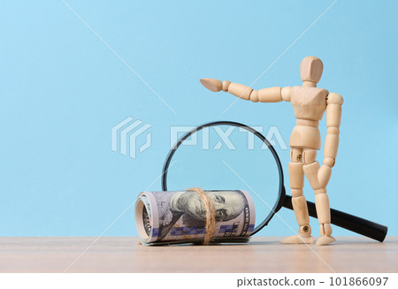 Wooden mannequin, magnifying glass and tied paper american dollars on a blue background, the concept of income growth Wooden mannequin, magnifying glass and tied paper american dollars on a blue background, the concept of income growth 101866097