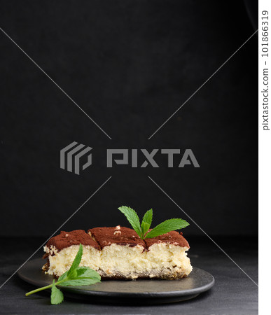 A piece of tiramisu sprinkled with cocoa, on top of a sprig of fresh mint on a black background A piece of tiramisu sprinkled with cocoa, on top of a sprig of fresh mint on a black background 101866319