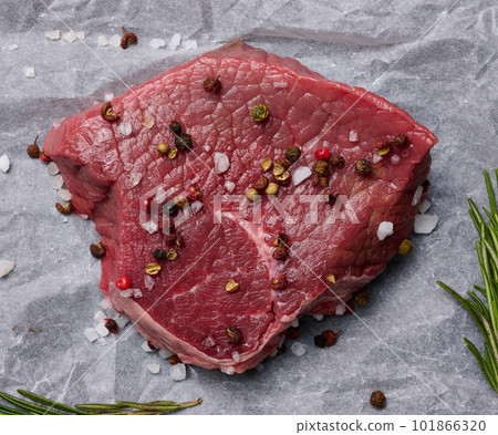 Raw piece of beef with spices lies on a white piece of parchment paper, top view Raw piece of beef with spices lies on a white piece of parchment paper, top view 101866320