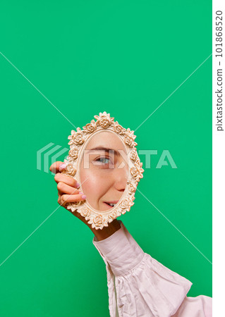 Graceful female hand holding small mirror with reflection of beautiful girl's eye glowing with joy over bright blue background. Happiness, joy Graceful female hand holding small mirror with reflection of beautiful girl's eye glowing with joy over bright blue background. Happiness, joy 101868520