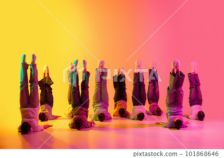 Group of pretty teenage girls wearing white t-shirt and jeans dancing together on pink and yellow gradient background in neon light. Synchronicity 101868646