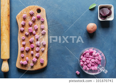 Beetroot and potato homemade gnocchi on wooden cutting board and in a glass mug, ingredients, sage leaf, rolling pin, dark blue background, top view Beetroot and potato homemade gnocchi on wooden cutting board and in a glass mug, ingredients, sage leaf, rolling pin, dark blue background, top view 101870741