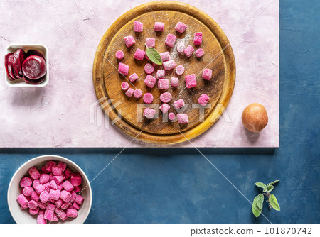 Beetroot and potato homemade gnocchi on round wooden cutting board and in a bowl, ingredients, sage leaf, dark blue and pink backgrounds, top view Beetroot and potato homemade gnocchi on round wooden cutting board and in a bowl, ingredients, sage leaf, dark blue and pink backgrounds, top view 101870742