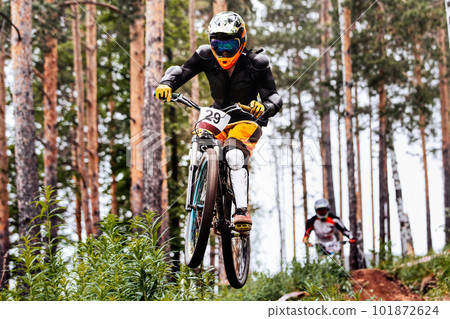 male racer athlete riding downhill race, jump over hill, on him protection jacket, and knee, shin guard 101872624