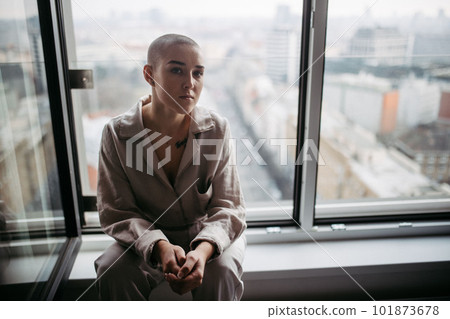 Young unhappy woman with cancer sitting in a window and looking at view. 101873678