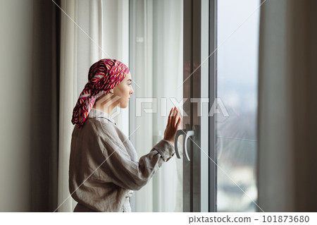 Young unhappy woman with cancer standing in front of a window. 101873680