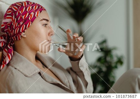 Portrait of young woman with cancer drinking water and lying in her bed, cancer awareness concept. 101873687