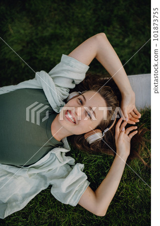 Young woman resting in city park, enjoying music trough headphones. 101873755
