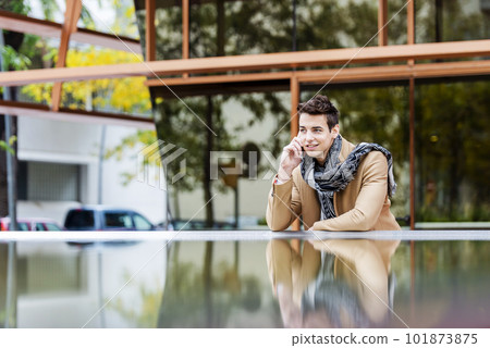 Portrait of stylish handsome young man with coat standing outdoors and leaning on wall using a smartphone Portrait of stylish handsome young man with coat standing outdoors and leaning on wall using a smartphone 101873875