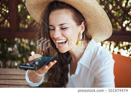 happy stylish woman in shirt sitting at table talking on phone 101874474
