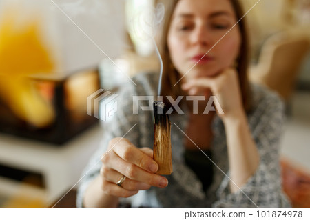 Woman hands burning Palo Santo, before ritual on the table with candles and green plants. Smoke of smudging treats pain and stress, clears negative energy and meditation wooden stick.. Woman hands burning Palo Santo, before ritual on the table with candles and green plants. Smoke of smudging treats pain and stress, clears negative energy and meditation wooden stick.. 101874978