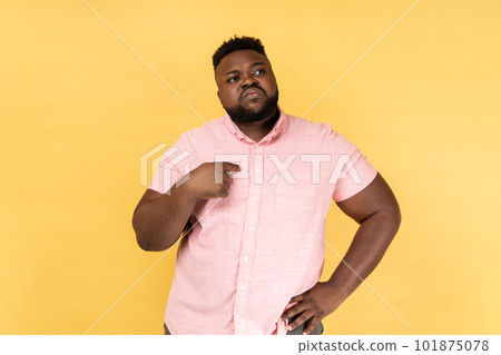 Portrait of young adult bearded man wearing pink shirt pointing fingers on himself and looking away with pride, extremely confident. Indoor studio shot isolated on yellow background. 101875078