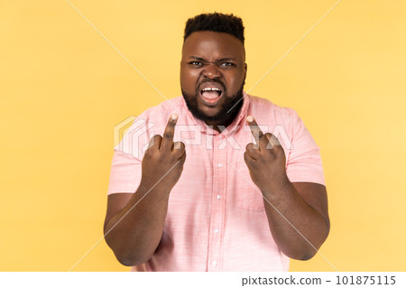Portrait of impolite aggressive man wearing pink shirt showing middle fingers and asking to get off expressing negativity, disrespectful behaviour. Indoor studio shot isolated on yellow background. 101875115