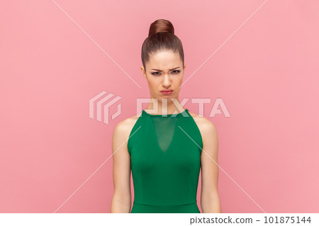 Portrait of unhappy stressed depressed woman looking at camera with frowning face, feels soul pain, expressing sorrow, wearing green dress. Indoor studio shot isolated on pink background. 101875144