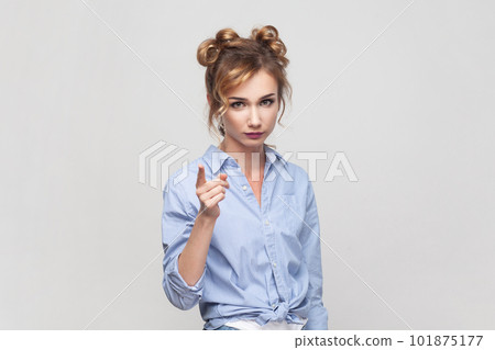 Hey, listen me attentively. Portrait of blonde woman raising index finger, looking with angry expression, warning you about danger, wearing blue shirt. Indoor studio shot isolated on gray background. Hey, listen me attentively. Portrait of blonde woman raising index finger, looking with angry expression, warning you about danger, wearing blue shirt. Indoor studio shot isolated on gray background. 101875177