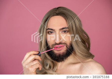 Transgender wearing blonde wig and white dress doing makeup applying lip gloss preparing for party Transgender wearing blonde wig and white dress doing makeup applying lip gloss preparing for party 101875188