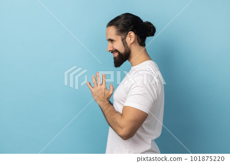 Side view of devious man with beard wearing white T-shirt smirking and conspiring cunning sly plan, pondering tricky clever idea in mind, wants to cheat. Indoor studio shot isolated on blue background Side view of devious man with beard wearing white T-shirt smirking and conspiring cunning sly plan, pondering tricky clever idea in mind, wants to cheat. Indoor studio shot isolated on blue background 101875220