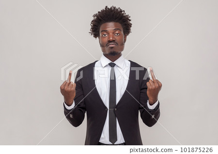 Impolite displeased man with Afro hairstyle shows middle finger, being angry with someone, purses lips frowns furious, wearing white shirt and tuxedo. Indoor studio shot isolated on gray background. 101875226
