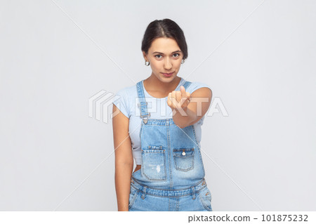 Come here. Portrait of attractive woman wearing denim overalls gesturing come to me, beckoning with finger, inviting for confidential talk. Indoor studio shot isolated on gray background. 101875232