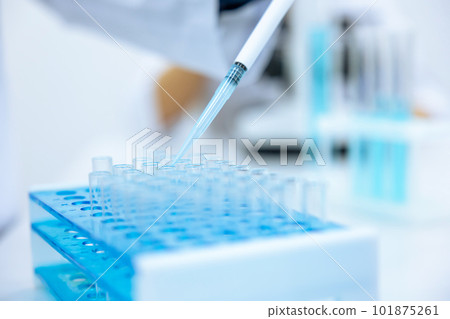 Unrecognizable scientist dripping blue liquid from pipette into test tube at table in laboratory. 101875261