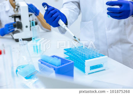 Unrecognizable scientist dripping blue liquid from pipette into test tube at table in laboratory. Unrecognizable scientist dripping blue liquid from pipette into test tube at table in laboratory. 101875268