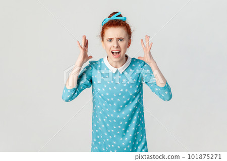 Portrait of angry depressed ginger woman arguing with her husband, screaming with hate and anger, being aggressive, wearing blue dress. Indoor studio shot isolated on gray background. 101875271