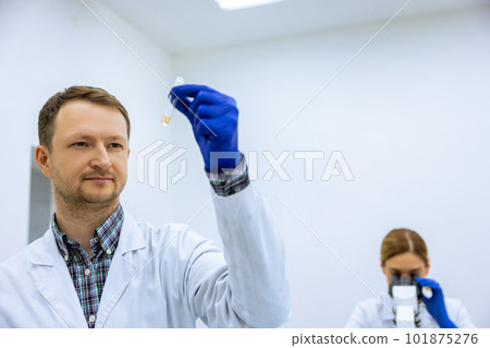 Male scientist analyzes liquid female researcherworking with microscope investigating medical sample Male scientist analyzes liquid female researcherworking with microscope investigating medical sample 101875276