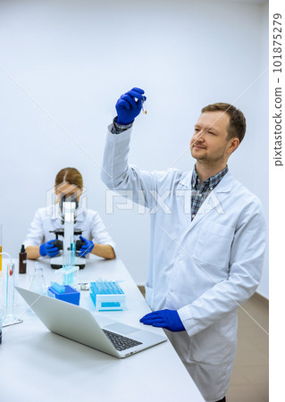 Male scientist analyzes liquid in beaker and types down observations on computer Male scientist analyzes liquid in beaker and types down observations on computer 101875279