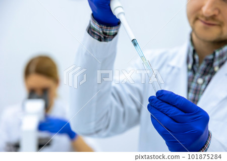 Male scientist analyzes liquid female researcherworking with microscope investigating medical sample 101875284