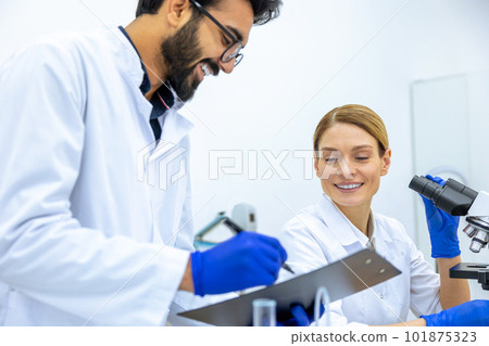 Woman and man scientists in lab coat making notes after doing sample test in laboratory. Woman and man scientists in lab coat making notes after doing sample test in laboratory. 101875323