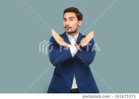 Serious strict man with mustache standing showing x sign, no way gesture, looking at camera with bossy expression, wearing official style suit. Indoor studio shot isolated on light blue background. 101875373