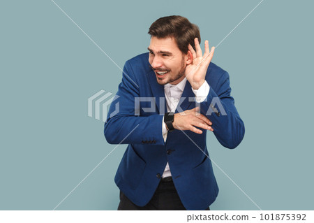 Portrait of handsome man standing with frowning face and hand near ear, trying to listen silent conversation, wearing official style suit. Indoor studio shot isolated on light blue background. 101875392