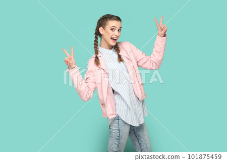 Portrait of excited optimistic cheerful teenager girl with braids wearing pink jacket showing v signs, being happy, being in high spirit. Indoor studio shot isolated on green background. Portrait of excited optimistic cheerful teenager girl with braids wearing pink jacket showing v signs, being happy, being in high spirit. Indoor studio shot isolated on green background. 101875459