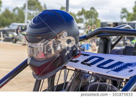 A well-worn helmet hanging on a speedway race car in the pits 101875633