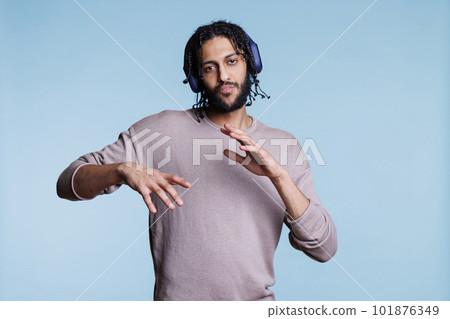 Confident arab man making cool moves while listening to music in headphones and looking at camera. Young person dancing while enjoying songs playlist in earphones portrait 101876349