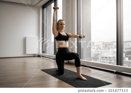 Strong woman using dumbbells for training on yoga mat 101877313