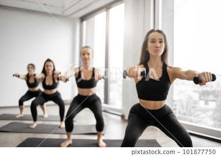 Ladies doing squats with dumbbells in modern yoga centre Ladies doing squats with dumbbells in modern yoga centre 101877750