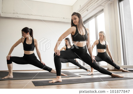 Females taking standing yoga posture in meditation room 101877847