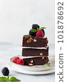 close-up of delicious chocolate brownie square pieces with hazelnuts, decorated with raspberries and blackberries. traditional homemade dessert. Gray background. vertical image 101878692