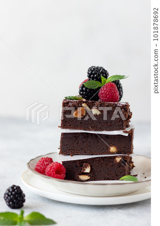 close-up of delicious chocolate brownie square pieces with hazelnuts, decorated with raspberries and blackberries. traditional homemade dessert. Gray background. vertical image 101878692