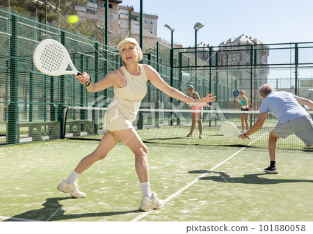 Mature sporty woman playing padel game in court on sunny day 101880058