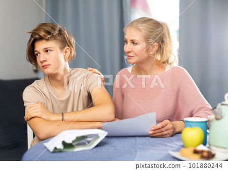 Frustrated teenage boy with worried mother reading paper letter Frustrated teenage boy with worried mother reading paper letter 101880244