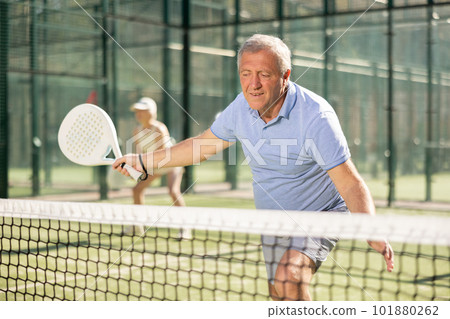 Determined sporty older man doing his best playing padel in court 101880262