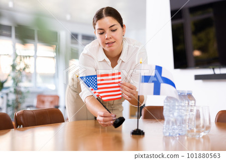 Young female assistant putting up finnish and american flags on table for international negotiations 101880563