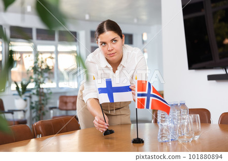Positive young woman putting flag of Finland on the table with flag of Norway in conference room 101880894